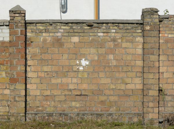 Brick fence texture made up of bricks in various shades of tan and brown, with a strip of grey cement with brick fragments near the bottom.